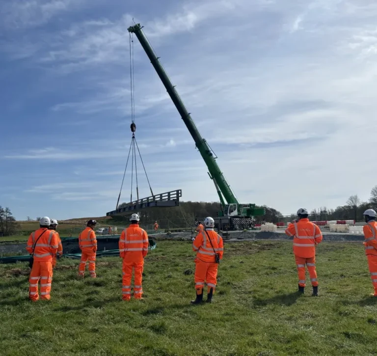 Roadworks crew watching a crane lift a bridge section into place
