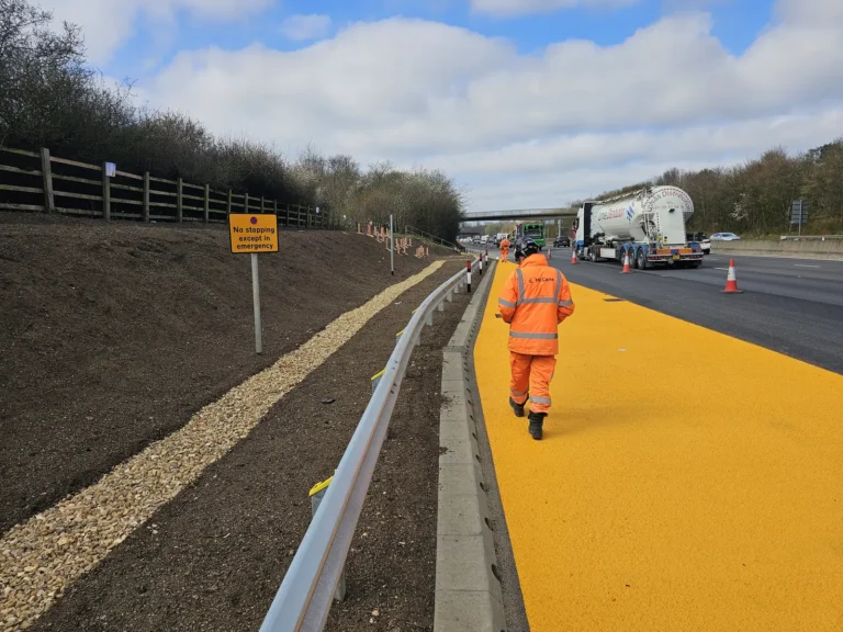 Roadworker walking along a freshly surfaced verge beside a busy motorway