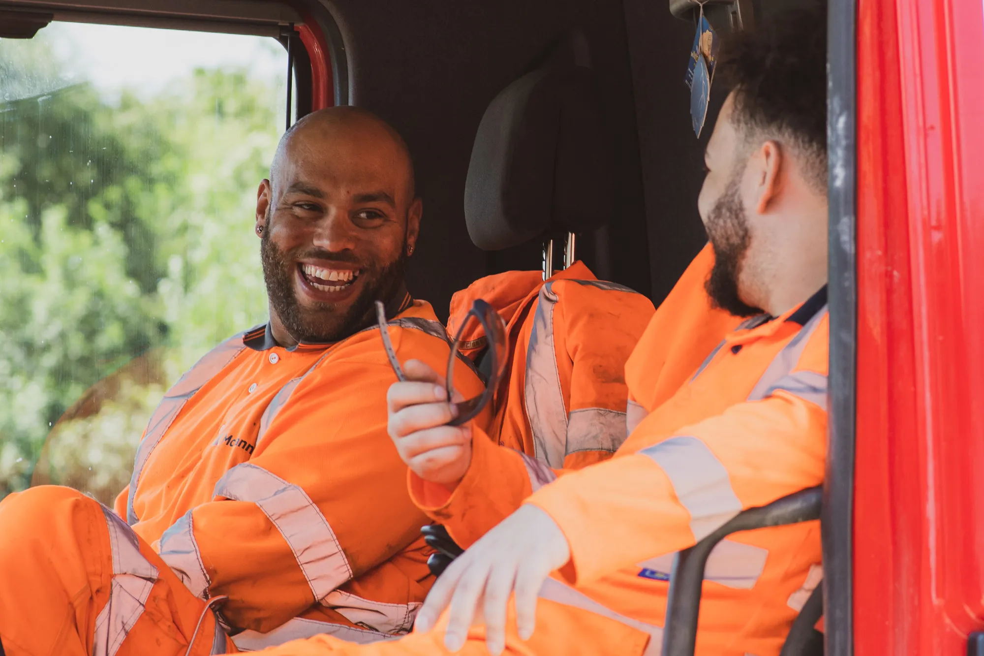 Two roadworkers in hi-vis sharing a laugh in a red works van