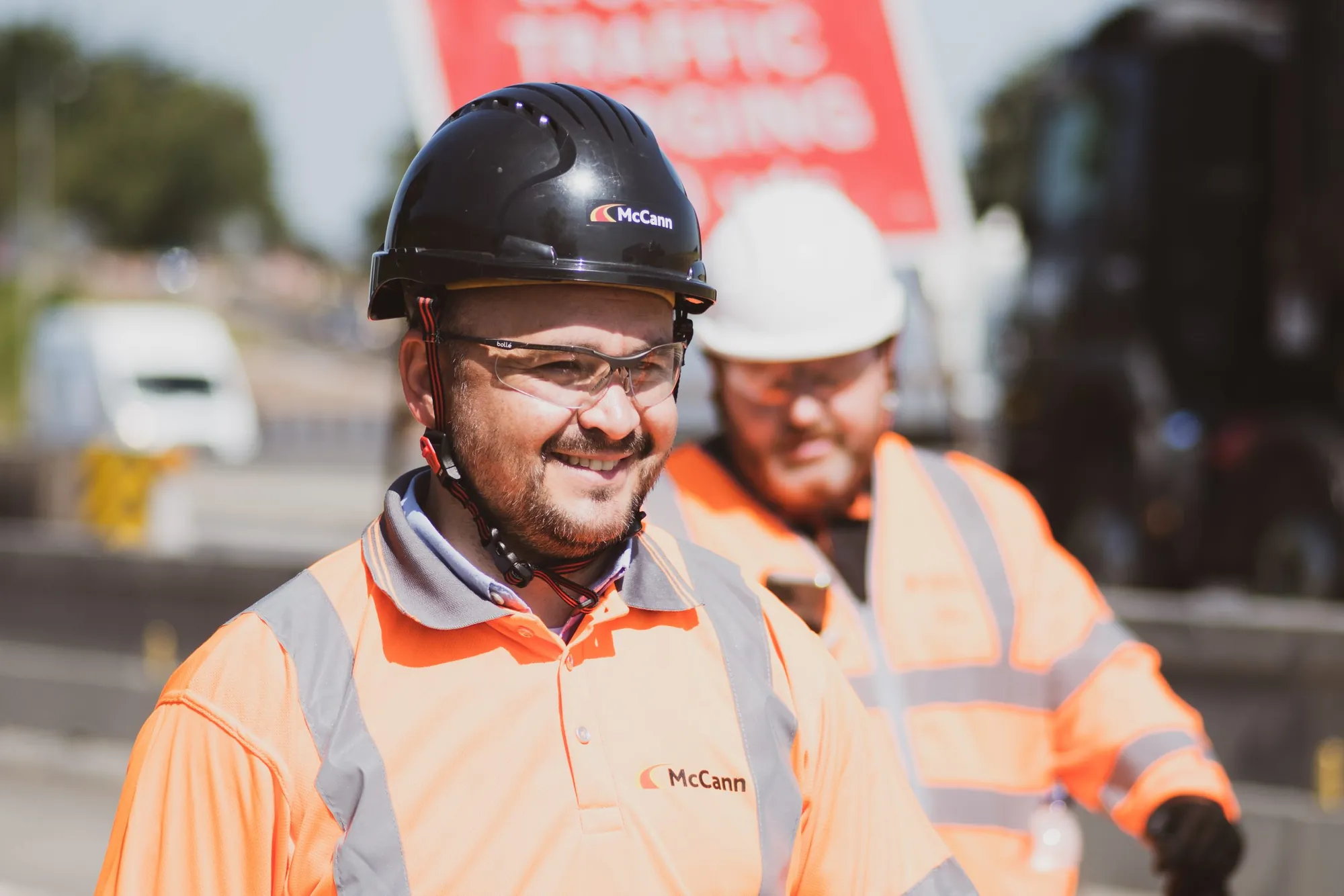 Smiling traffic management operative in a black helmet and hi-vis at a roadside site